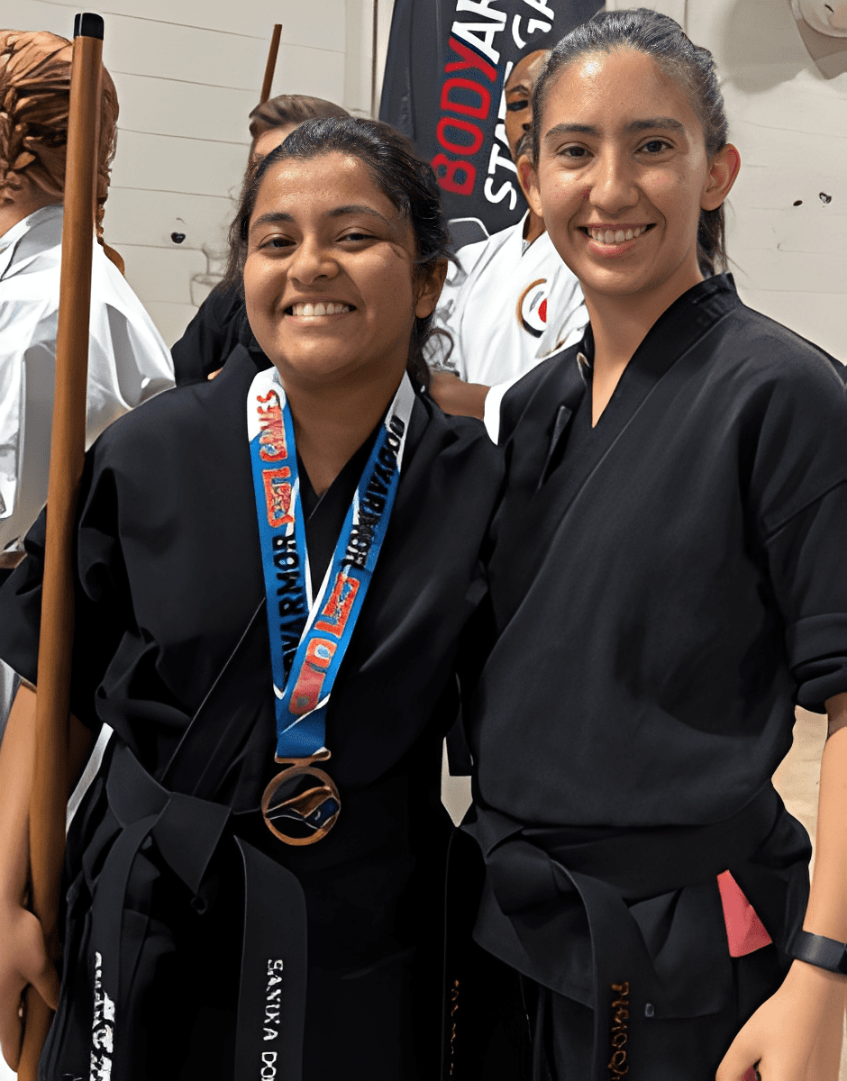 Two smiling martial artists in black uniforms, one wearing a medal.