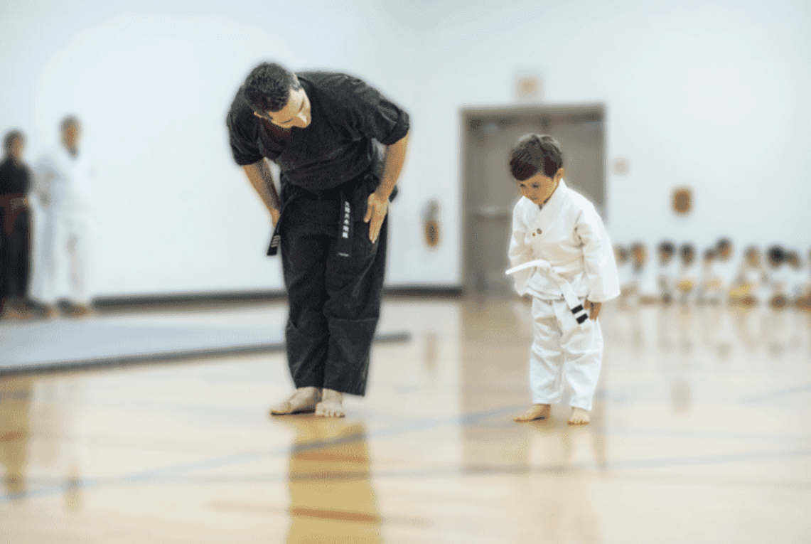 A martial arts instructor and child bowing in a dojo.