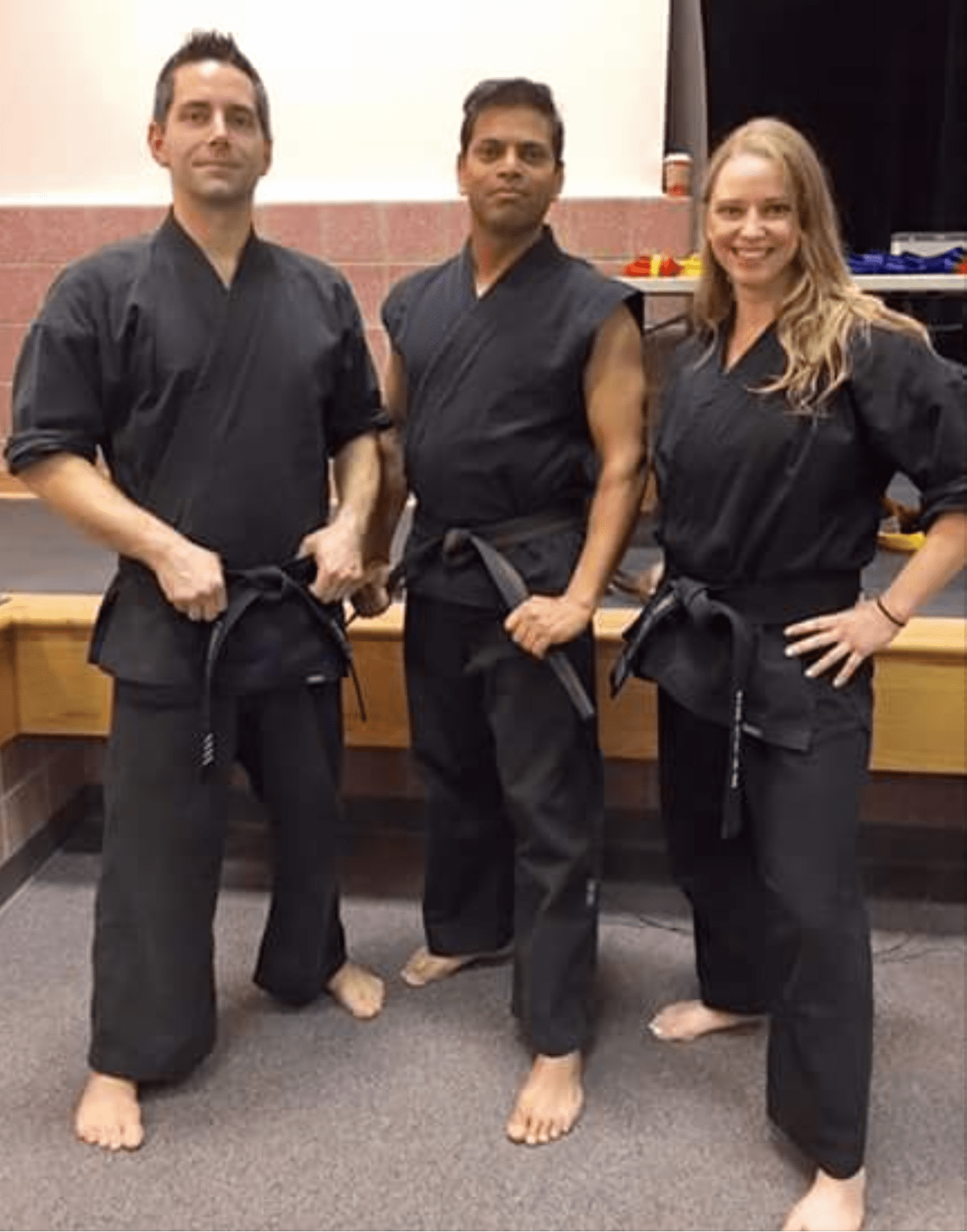 Three people in black karate uniforms posing with belts.