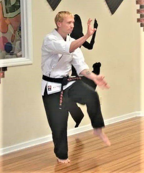 A martial artist practicing a high kick indoors.