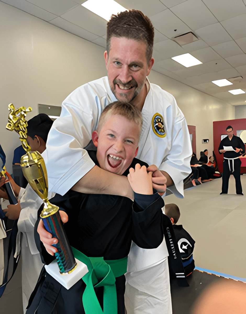 A happy child holding a trophy with a martial arts instructor behind him.
