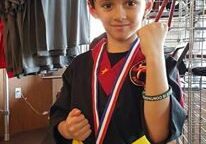 Boy showing medal, wearing martial arts gear.